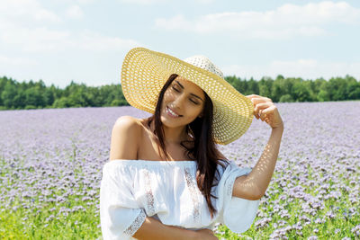Young woman wearing hat standing on field against sky