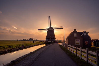 Traditional windmill on landscape against sky during sunset