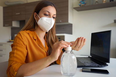 Young woman wearing mask using hand sanitizer at home