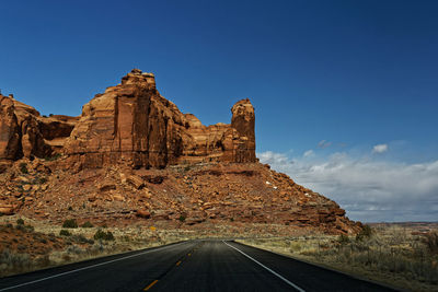 Road leading towards rock formation against sky