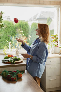 Woman in kitchen throwing fresh red pepper