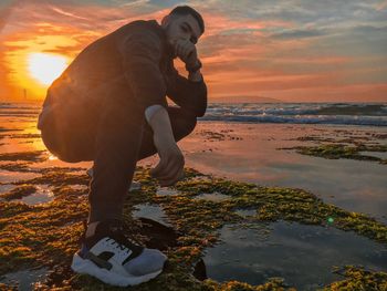 Man standing on beach against sky during sunset