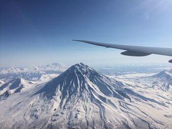 Cropped image of aircraft wing over snow covered mountains against sky