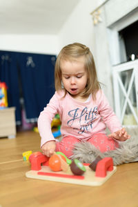 2 year old baby girl at home cutting woden toy fruits with wooden knife. child development concept