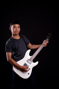 Low section of man holding guitar against black background