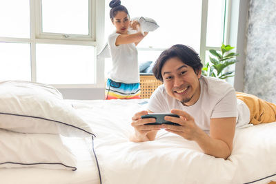 Smiling young woman using smart phone while sitting on bed at home