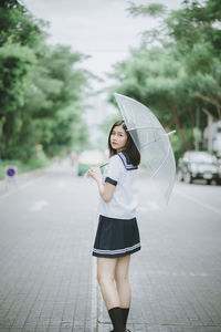 Portrait of young woman with umbrella standing on road