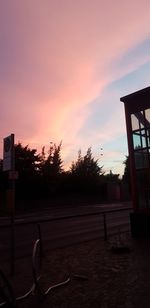 Silhouette trees by street against sky at sunset