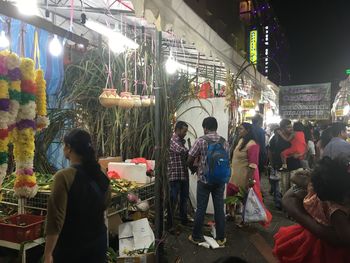 Rear view of people standing in illuminated market at night