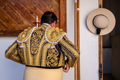Back view of anonymous picador getting ready for bullfighting putting on traditional shiny costume in stable