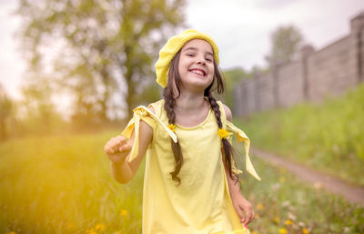 Cheerful and happy charming little girl in a yellow  beret and a yellow dress, dancing in nature 