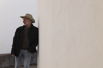 Portrait of adult man in cowboy hat and jeans against wall.