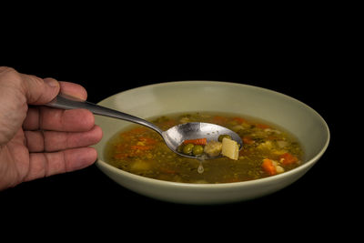 Cropped hand holding soup in bowl on table