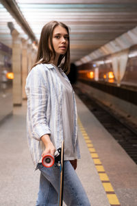 Young girl with longboard wait for train at metro station. female at underground platform with skate