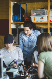 Mature female teacher looking at male high school student preparing science project in classroom