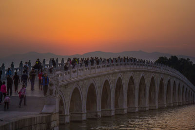 People at bridge against sky during sunset