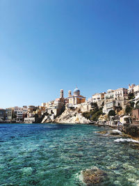 Buildings by sea against blue sky