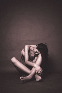 Young woman sitting against wall