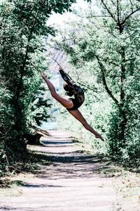 Full length of woman dancing over footpath amidst trees