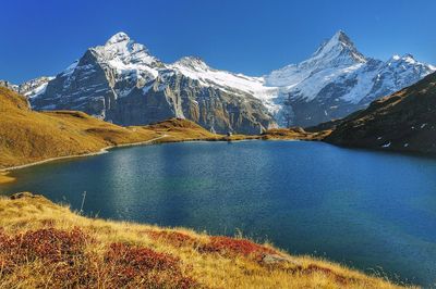 Scenic view of lake and snowcapped mountains against clear blue sky