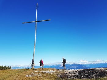 People standing by cross on mountain against clear blue sky