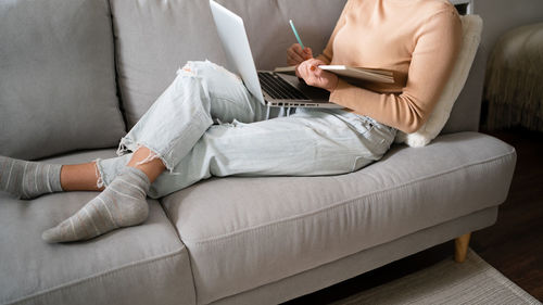 Midsection of woman using laptop while sitting on sofa at home
