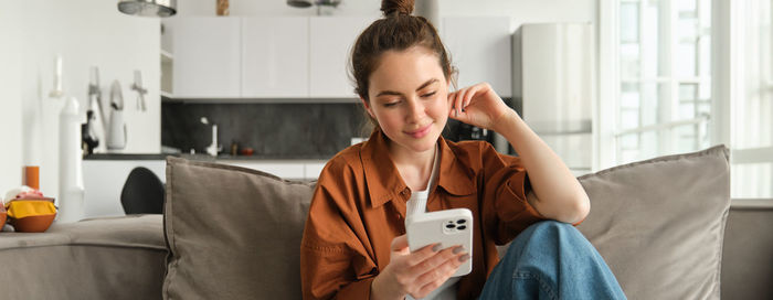 Young woman using mobile phone while sitting at home