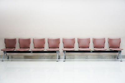 Empty chairs in row against white wall