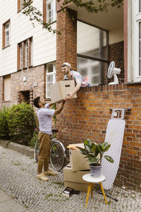 Gay couple helping each other holding cardboard box during relocation of house