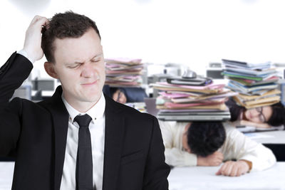 Sad businessman scratching head against tired colleagues