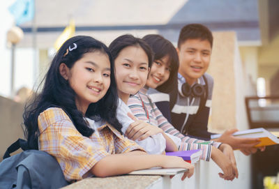 Portrait of smiling friends standing by retaining wall