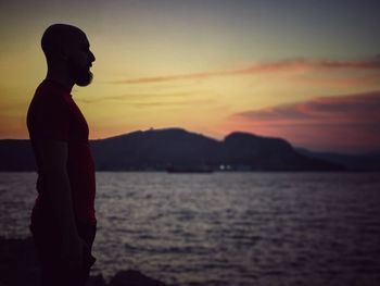 Silhouette man looking at sea against sky during sunset