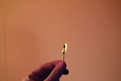 Cropped hand holding burning matchstick against brown wall