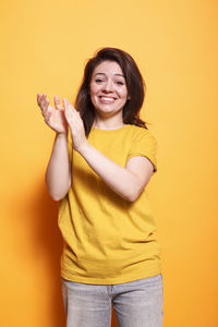 Young woman with arms raised standing against yellow background