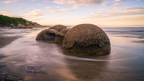 Scenic view of rocks on beach against sky during sunset