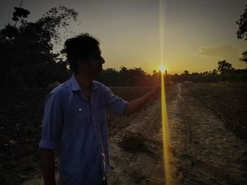 Young man standing on land against sky during sunset