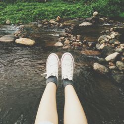 Low section of woman standing on rock by water