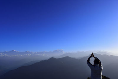 Rear view of man practicing yoga on mountain against clear blue sky