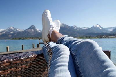 Low section of person relaxing on wicker by lake