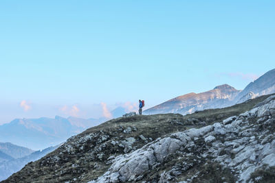 Distant view of male hiker standing on cliff against blue sky