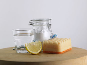 Close-up of baking soda in glass jar vinegar and lemon on table