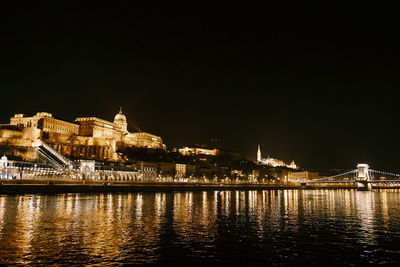 Illuminated buildings by river against sky at night