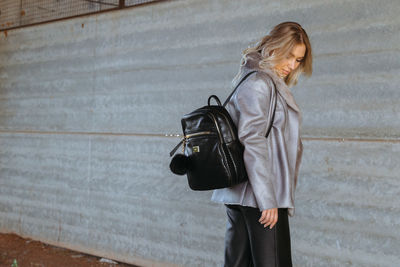 Young woman carrying bag standing against wall