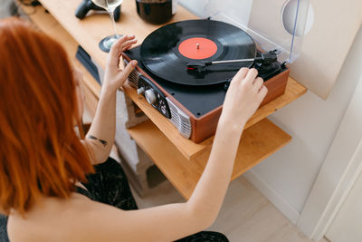 From above side view of crop anonymous female turning on retro record player on shelf in house