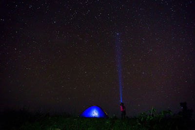 Woman with illuminated flashlight and tent against star field at night