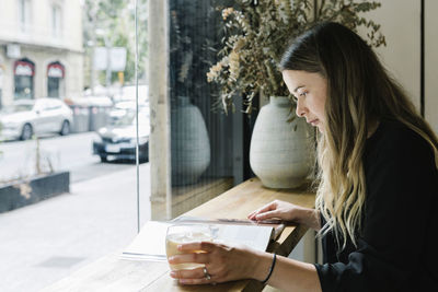 Businesswoman reading magazine while drinking coffee at coffee shop