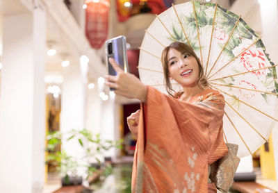 Smiling woman wearing traditional clothing taking selfie outdoors