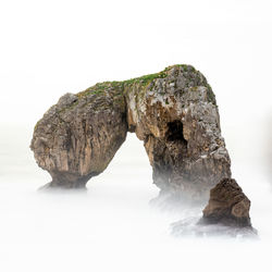 Rock formation in sea against clear sky