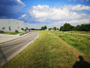 Road amidst grassy field against sky