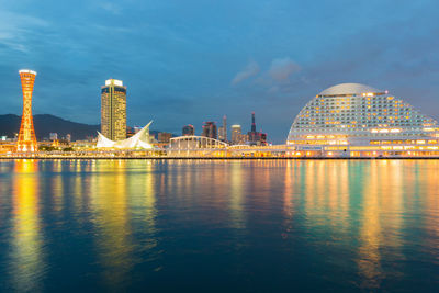 Illuminated city by sea against sky at night